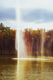 Fototapeta Tęcza - fountain spraying water against the background of autumn forest