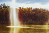 Fototapeta Tęcza - fountain spraying water against the background of autumn forest