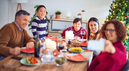 Beautiful family smiling happy and confident. Eating roasted turkey make selfie by smartphone celebrating christmas at home