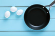 White chicken eggs and a cooking pan on blue wooden table. Cooking egg
