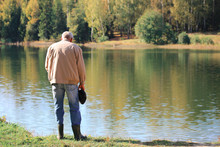 An Elderly Man Stands On The Shore And Looks Into The Water