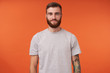 © timtimphoto - Attractive young bearded tattooed brunette man with trendy haircut standing over orange background, keeping hands along body and looking at camera with charming smile