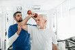 senior man lift a dumbbell, he doing treatment exercise with his physiotherapist. Physio treatment at rehab center