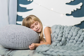 the little girl lies sleeping on a pillow covered with a gray knitted blanket, against the backgroun