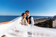 © maxbelchenko - Newlyweds enjoy each other tenderly in the shadow of a flying veil on the background of a beautiful sea landscape. The bride and groom hugging and kissing on the background of the sea.