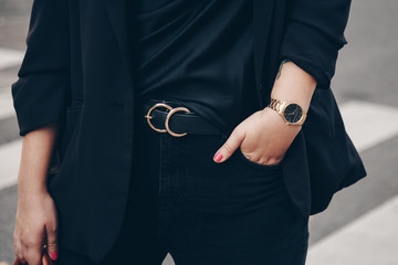 street style 2019 fashion details. close up, young fashion blogger wearing black jeans, satin top, blazer and a black and golden analog wrist watch. 