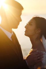 Beautiful bride and stylish groom together on the bridge against the background of the boat at sunset. Newlyweds tenderly hug, kiss and enjoy each other at sunset. Wedding. Love. Romantic moment. 