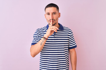 Wall Mural - Young handsome man wearing nautical striped t-shirt over pink isolated background asking to be quiet with finger on lips. Silence and secret concept.