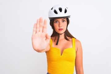 Wall Mural - Young beautiful cyclist girl wearing bike helmet standing over isolated white background with open hand doing stop sign with serious and confident expression, defense gesture