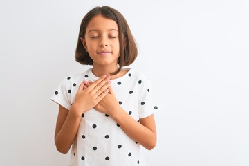 Canvas Print - Young beautiful child girl wearing casual t-shirt standing over isolated white background smiling with hands on chest with closed eyes and grateful gesture on face. Health concept.