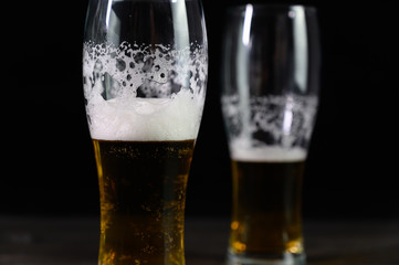 Photo of beer in two glasses. Thick foam and a nice color drink on a black background.