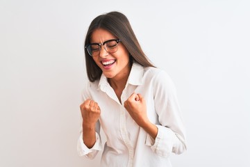 Poster - Young beautiful businesswoman wearing glasses standing over isolated white background very happy and excited doing winner gesture with arms raised, smiling and screaming for success