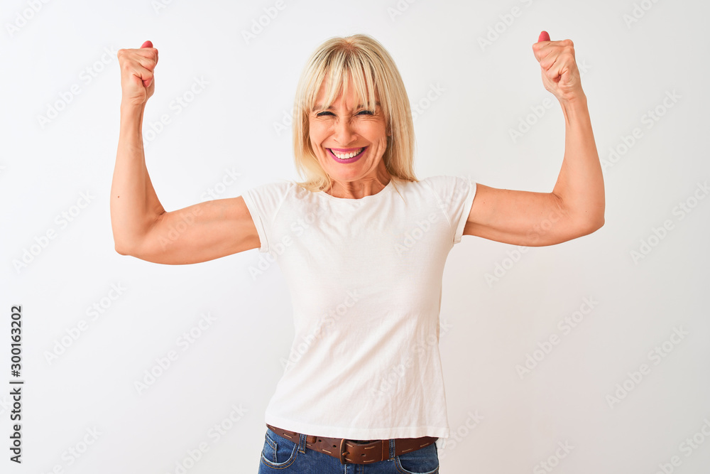 Middle age woman wearing casual t-shirt standing over isolated white background showing arms muscles smiling proud. Fitness concept. - obrazy, fototapety, plakaty 