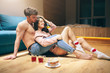 Young sexy couple after intimacy in kitchen in night.Hot lovely people enjoying each other. Woman sit on man's legs and smile. Shirtless guy look at model. Cups of tea and cakes on floor.
