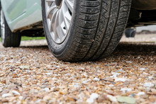 Ground Level View Of A New Car, Showing The Rear Tyre And Tread Together With The Alloy Wheel. Parked On A Gravel Driveway And Showing Some Of Its Light Blue Paint.