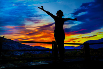 Wall Mural - Yoga body post silhouette of a women with arms raised in the light of the sunset sky background