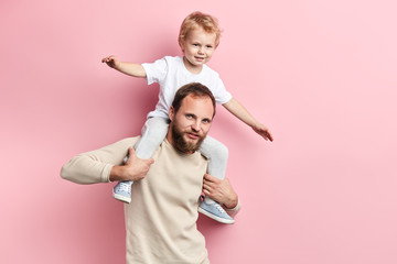 bearded man lifting his son , having great time. close up portrait, isolated pink background