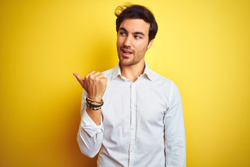 Sticker - Young handsome businessman wearing elegant shirt standing over isolated yellow background smiling with happy face looking and pointing to the side with thumb up.