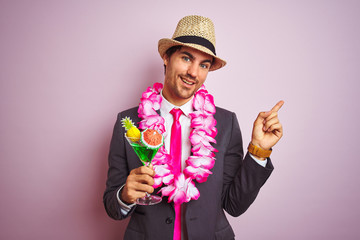 Sticker - Businessman wearing suit hat hawaiian lei drinking cocktail over isolated pink background very happy pointing with hand and finger to the side