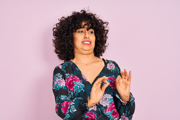 Sticker - Young arab woman with curly hair wearing floral dress over isolated pink background disgusted expression, displeased and fearful doing disgust face because aversion reaction. With hands raised