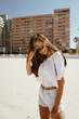 © mnelen.com - girl on the beach on the background of buildings, head down straightens her hair
