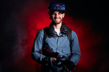 Wall Mural - Portrait of young cool man holding VR weapon, wearing casual clothes playing virtual game. Isolated over smoky background