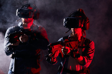 Two young male and female stand with weapons in smoky studio. Modern hi-tech