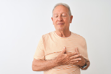 Canvas Print - Senior grey-haired man wearing striped t-shirt standing over isolated white background smiling with hands on chest with closed eyes and grateful gesture on face. Health concept.