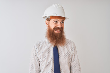 Sticker - Young redhead irish architect man wearing security helmet over isolated white background looking away to side with smile on face, natural expression. Laughing confident.