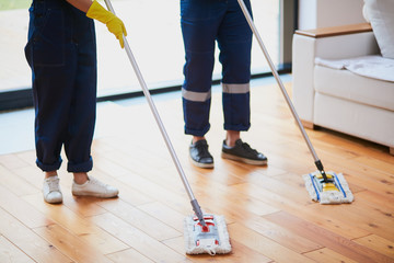 Closeup of janitors legs washing wooden floor with mops. Cleaning service concept