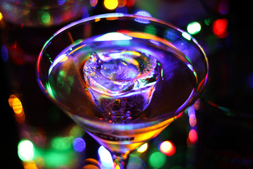 Viersen, Germany - November 2. 2019: View on glass with martini cocktail with ice cube. Vibrant colorful bokeh background.