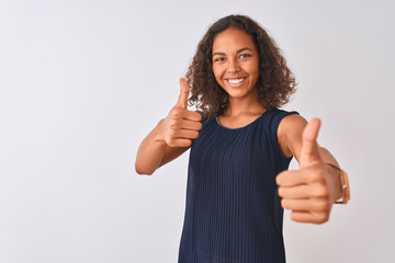 Wall Mural - Young brazilian woman wearing blue dress standing over isolated white background approving doing positive gesture with hand, thumbs up smiling and happy for success. Winner gesture.