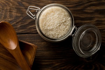 Wall Mural - White uncooked, raw long grain rice in glass storage jar on rustic brown wooden table top view flat lay from above