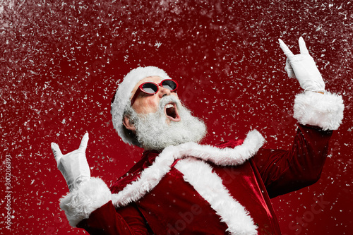 Fotografía Waist up portrait of cool rock Santa roaring over red background with snow falli