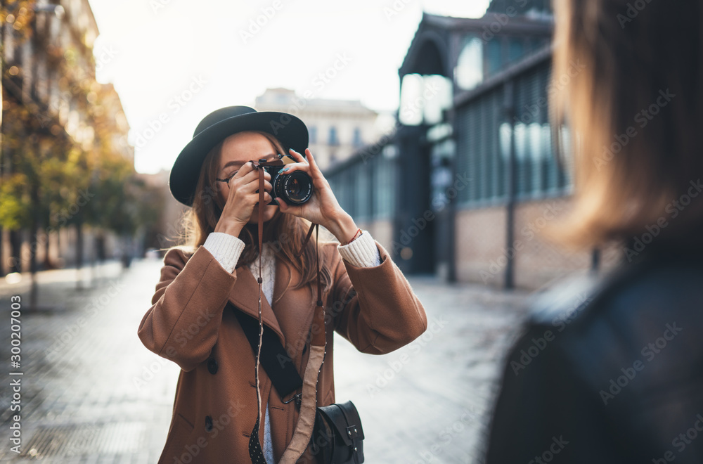 Outdoor smiling lifestyle portrait of pretty young woman having fun in sun city Europe autumn with camera travel photo of photographer Making pictures in glasses and hat with girlfriends - obrazy, fototapety, plakaty 