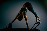 Young girl doing pilates exercises with a reformer bed. Beautiful slim fitness trainer on reformer gray background, low key, art light. Fitness concept