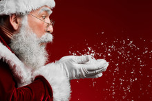 Side View Portrait Of Classic Santa Claus Blowing Snow While Standing Against Red Background, Copy Space
