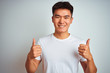 © Krakenimages.com - Young asian chinese man wearing t-shirt standing over isolated white background success sign doing positive gesture with hand, thumbs up smiling and happy. Cheerful expression and winner gesture.