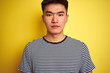 © Krakenimages.com - Young asian chinese man wearing striped t-shirt standing over isolated yellow background with a confident expression on smart face thinking serious
