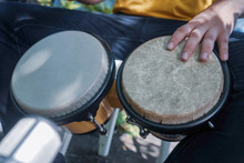  Sitting Playing Congas Outside. Drum Between The Legs. African Drums. Percussion Instrument Being Played Concept. Represented By Percussionists Hands Hitting A Drum.