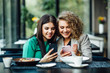 © Тарас Нагирняк - Young girls friends spending time together drinking coffee in the cafe, having breakfast and dessert. Youth, lifestyle, communication concept, using their phones.