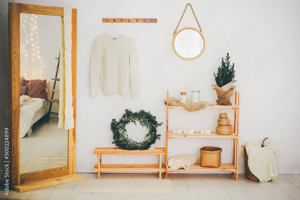 Scandinavian hallway interior with big mirror and shoe storage bench near white wall. Hallway with christmas decor. - obrazy, fototapety, plakaty 