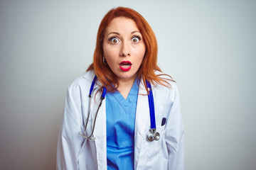 Sticker - Young redhead doctor woman using stethoscope over white isolated background afraid and shocked with surprise and amazed expression, fear and excited face.