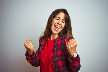 Wall Mural - Young beautiful woman wearing red t-shirt and jacket standing over white isolated background very happy and excited doing winner gesture with arms raised, smiling and screaming for success