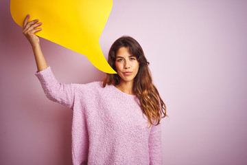 Wall Mural - Young beautiful woman holding yellow speech bubble standing over pink isolated background with a confident expression on smart face thinking serious