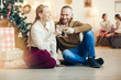 © Seventyfour - Full length portrait of happy couple clinking champagne glasses sitting by Christmas tree at home, copy space