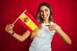 © Krakenimages.com - Young beautiful woman holding spanish flag over red isolated background with surprise face pointing finger to himself