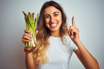 Wall Mural - Young beautiful woman eating asparagus over grey isolated background surprised with an idea or question pointing finger with happy face, number one