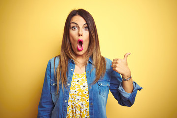 Canvas Print - Young beautiful woman standing over yellow isolated background Surprised pointing with hand finger to the side, open mouth amazed expression.