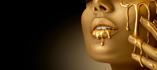 Wall Mural - Gold Paint smudges drips from the face lips and hand, lipgloss dripping from sexy lips, golden liquid drops on beautiful model girl's mouth, gold metallic skin make-up. Beauty woman makeup close up